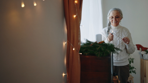 A senior woman lighting up candle at Christmas wreath indoors at home.