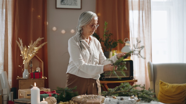 Senior woman a making Christmas wreath from natural materials indoors at home