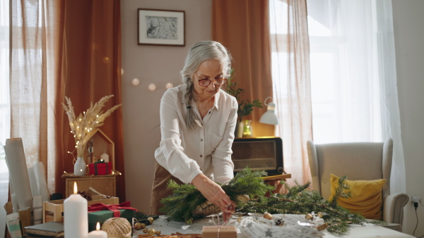 Senior woman a making Christmas wreath from natural materials indoors at home