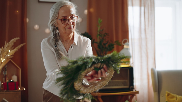 Senior woman a making Christmas wreath from natural materials indoors at home