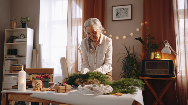 Senior woman a making Christmas wreath from natural materials indoors at home