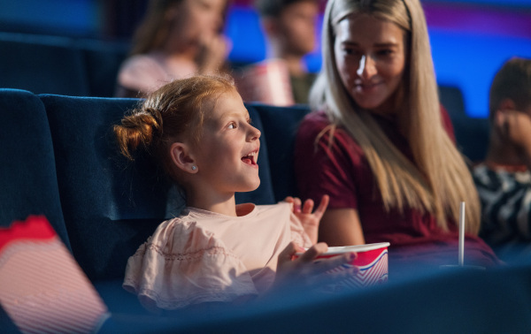 A happy small girl with mother in the cinema, watching film.