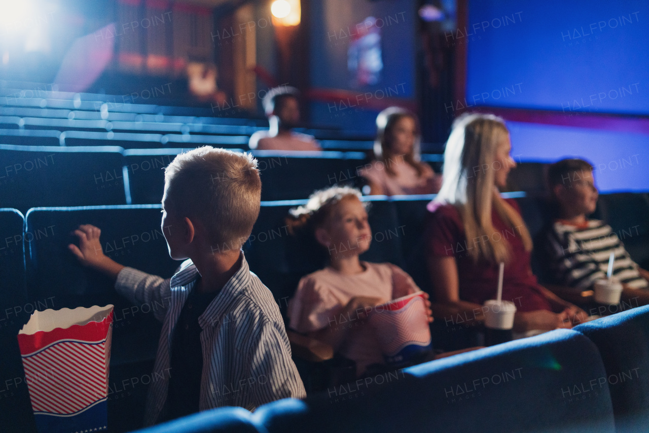 A mother with happy small children in the cinema, watching film.