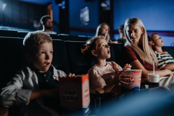 A mother with happy small children in the cinema, watching film.