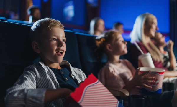 A small boy with family sitting and watching film in the cinema, eating popcorn