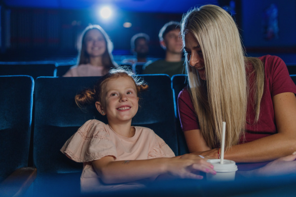 A happy small girl with mother in the cinema, watching film.