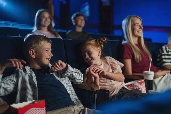 A mother with happy small children in the cinema, watching film and laughing.