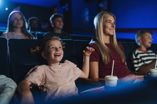 A mother with happy small children in the cinema, watching film.