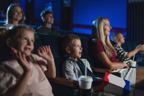 A mother with happy small children in the cinema, watching film.