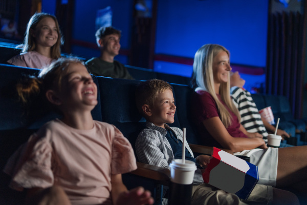 A mother with happy small children in the cinema, watching film and laughing.