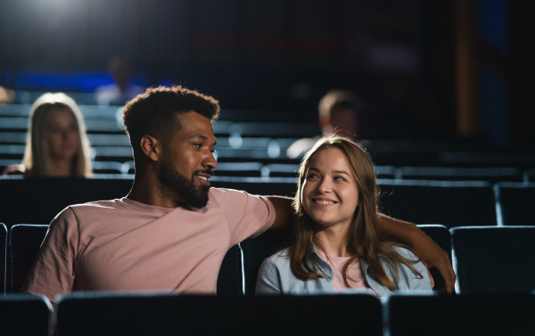 A front view of cheerful young couple in the cinema, watching film.