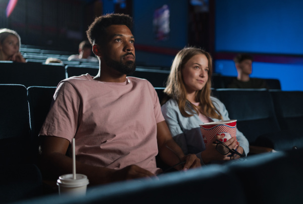 A cheerful young couple with popcorn in the cinema, watching film.