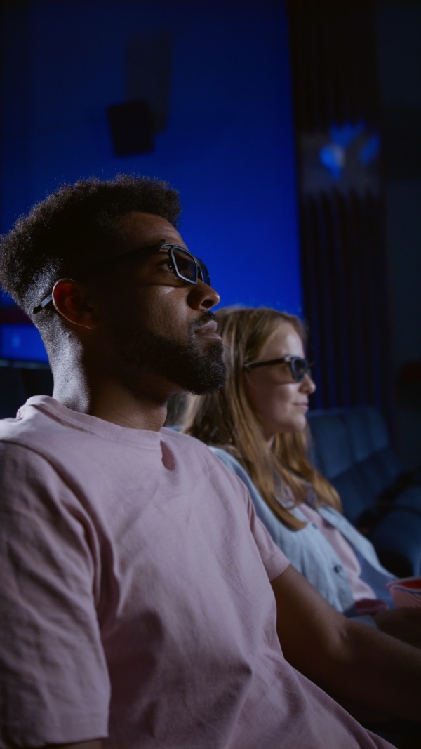 A vertical footage of cheerful young couple putting on 3d glasses in the cinema.