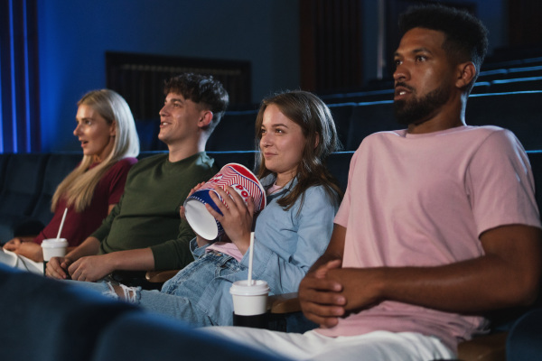 Young people with popcorn adn drinks in the cinema, watching a thriller film.