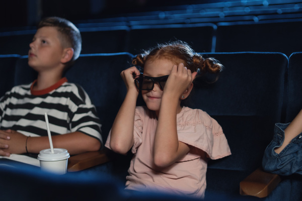 Happy small children with 3d glasses and popcorn in the cinema, watching film.