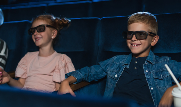 Happy small children with 3d glasses and popcorn in the cinema, watching film.