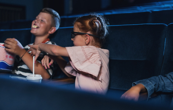 Small children with 3d glasses and popcorn in the cinema, watching a film.