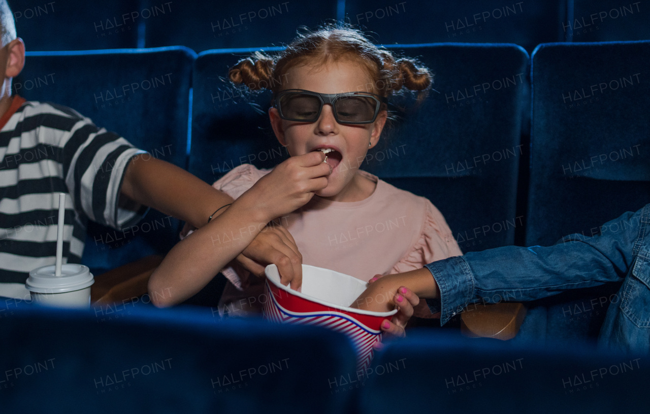 Happy small children with 3d glasses and popcorn in the cinema, watching film and eating popcorn.