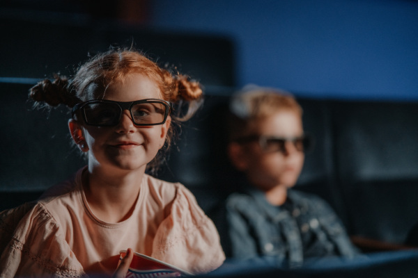 Small children with 3d glasses and popcorn in the cinema, watching film.