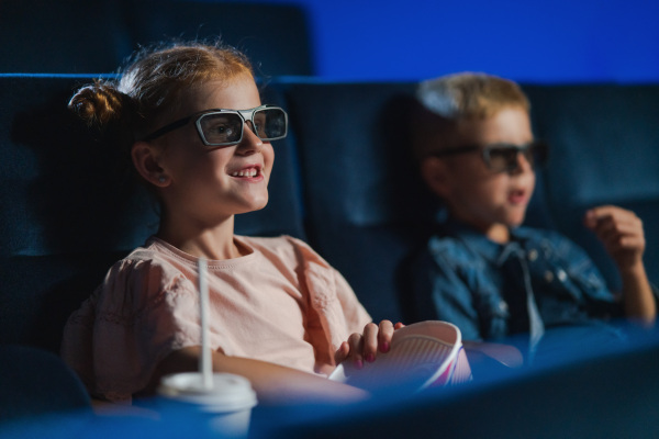 Small children with 3d glasses and popcorn in the cinema, watching film.