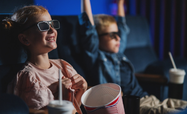 Small children with 3d glasses and popcorn in the cinema, watching a film.