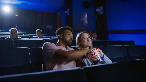 A cheerful young couple with popcorn in the cinema, talking.