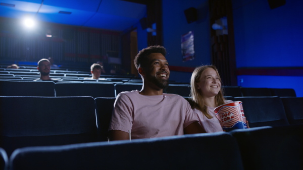 A cheerful young couple with popcorn in the cinema laughing and talking.