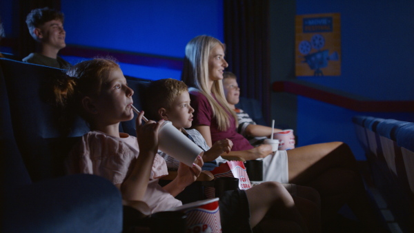 A mother with happy small children in the cinema, watching film.