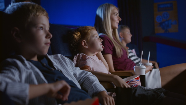 A mother with happy small children in the cinema, watching film.