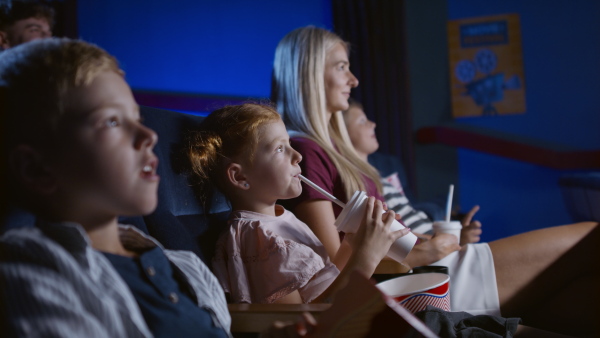 A mother with happy small children in the cinema, watching film.