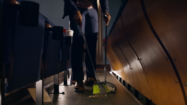 A unrecognizable young man cleaner sweeping floor in the cinema after the film.