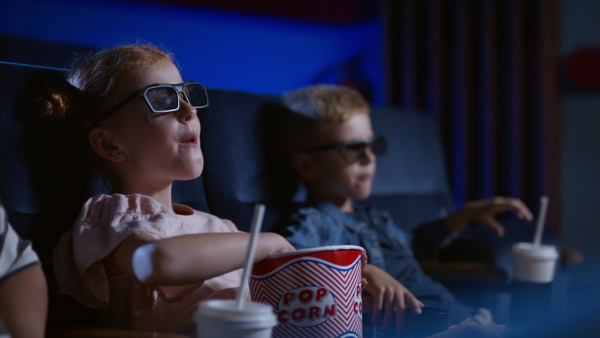 Happy small children with 3d glasses and popcorn in the cinema, watching film and eating popcorn.