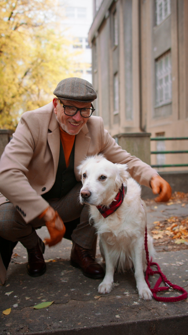 A vertical footage of happy senior man looking at camera during dog walk outdoors in city.