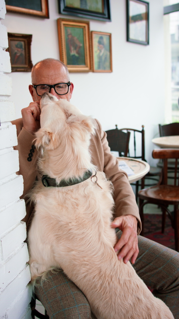 A vertical footage of happy senior man sitting in cafeteria and giving a treat to his dog.