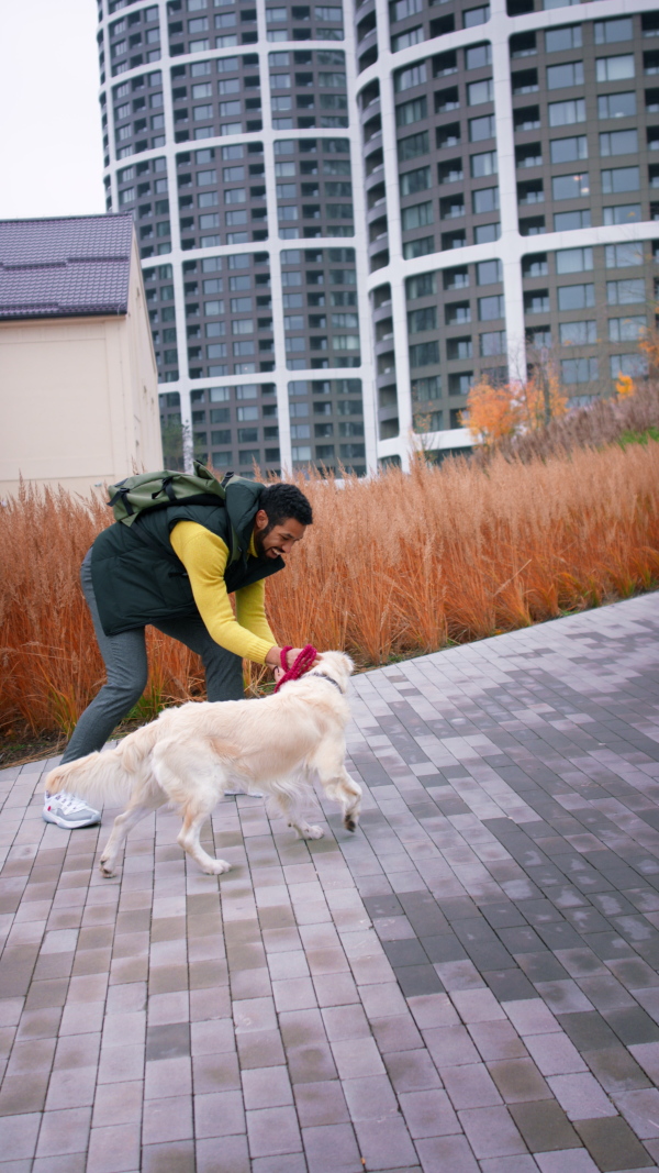 A vertical footage of happy young man running with his dog on leash outdoors in city.