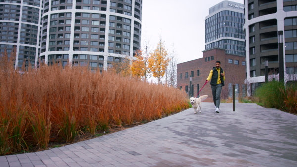 A happy young man running with his dog on leash outdoors in city.