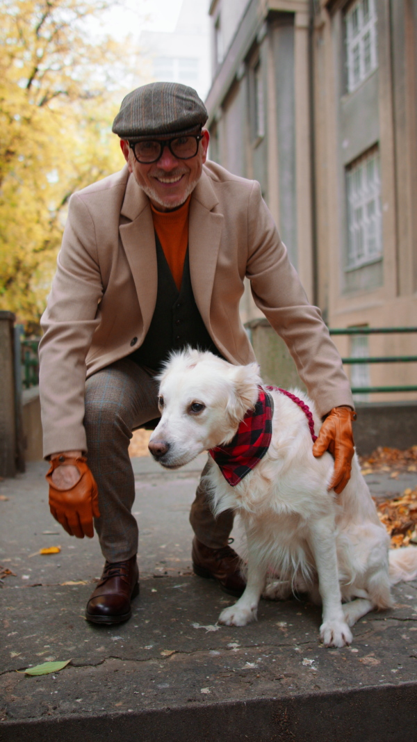 A vertical footage of happy senior man feeding his dog and looking at camera during walk outdoors in city.