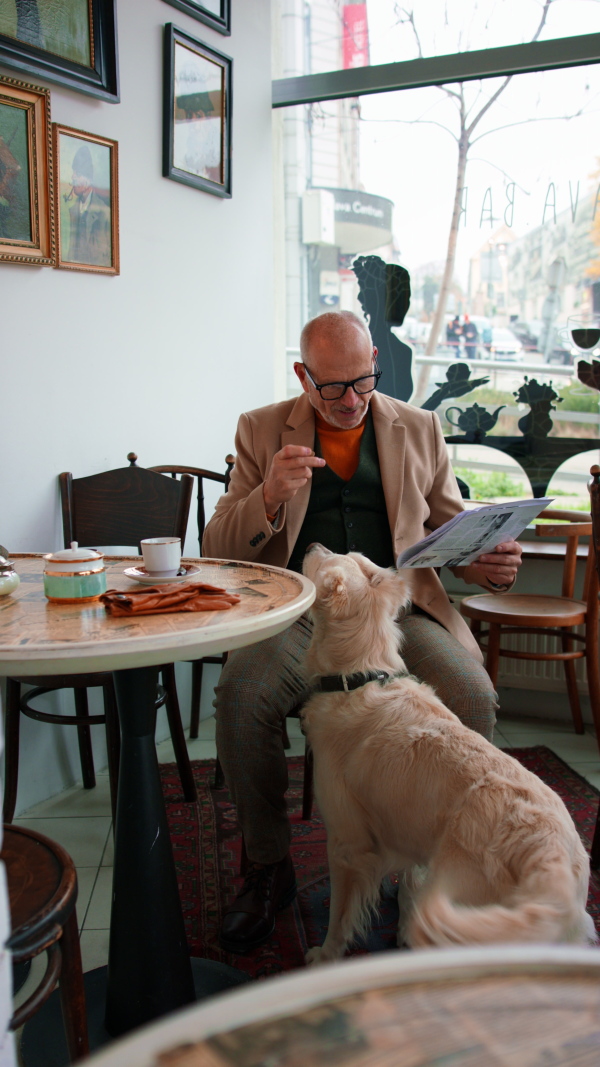 A vertical footage of happy senior man sitting in cafeteria and giving a treat to his dog.