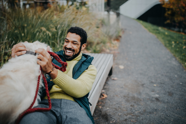 Happy young man training and cuddling with his dog outdoors in city park, during a cold autumn day.