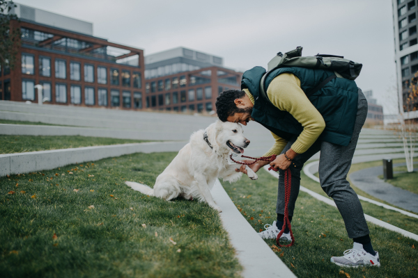 A side view of happy young man training his dog outdoors in city.