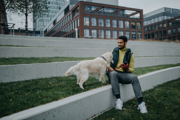 A happy young man lying on grass with his dog outdoors in town.