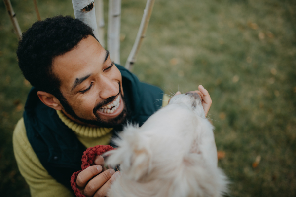 Happy young man training and cuddling with his dog outdoors in city park, during a cold autumn day.