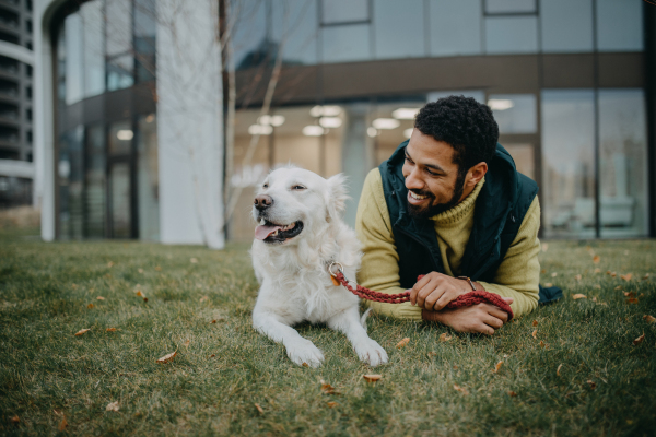 Happy young man resting with his dog outdoors in city park, during a cold autumn day.