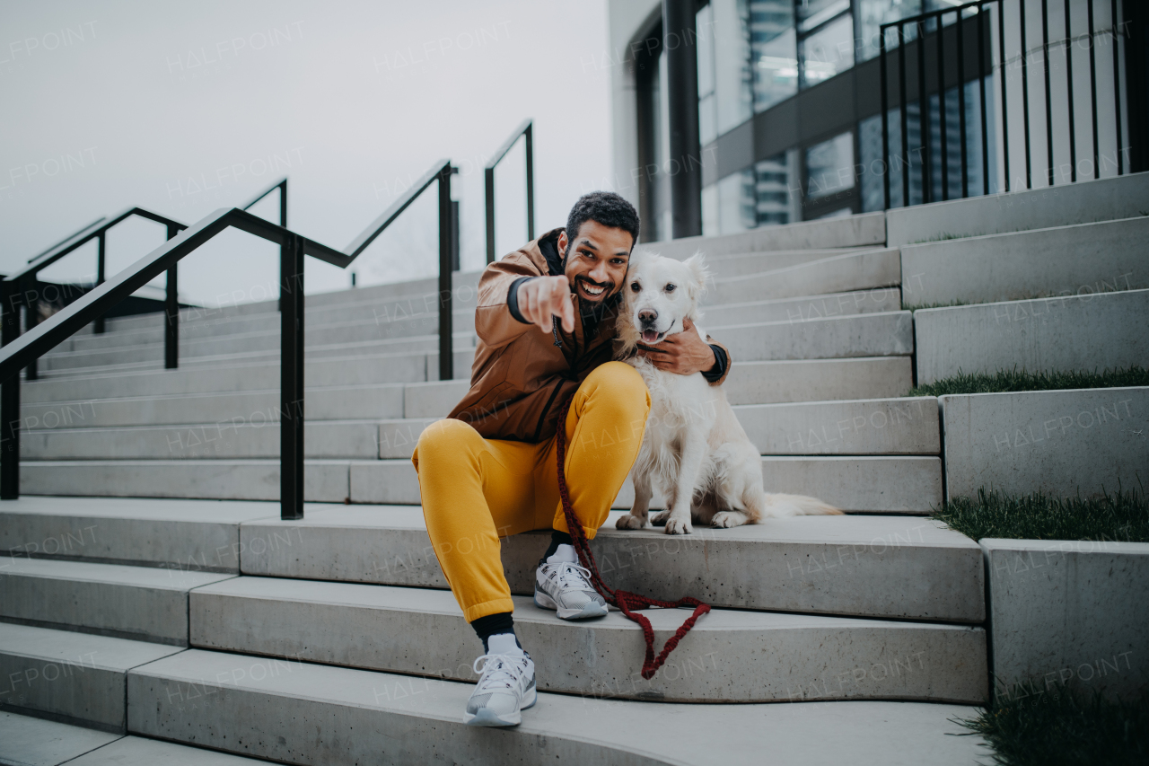 Portrait of happy young man and his dog outdoors in a city staircase, looking at camera.