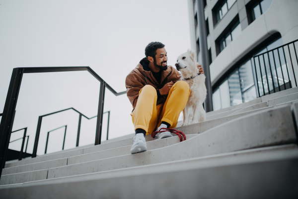 Low angle view of happy young man resting with his dog outdoors in city concrete staircase.