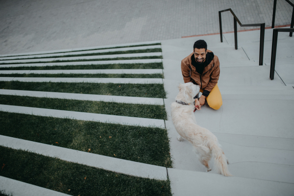 A high angle view of happy young man with his dog outdoors in city staircase.