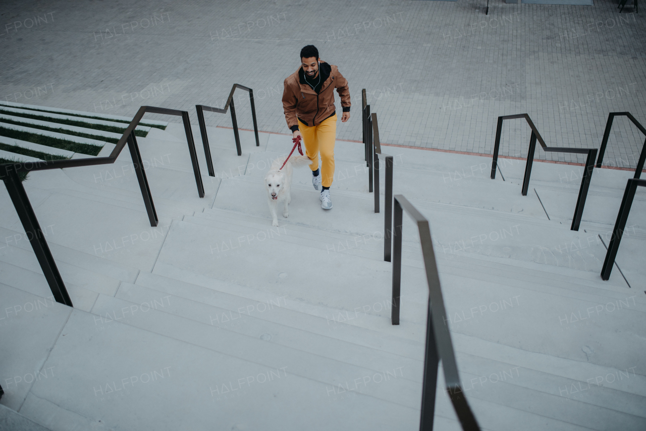 A high angle view of happy young man walking his dog outdoors in city.