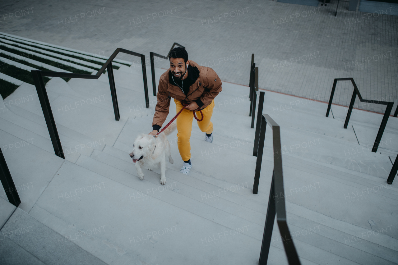 A high angle view of happy young man walking his dog outdoors in city.