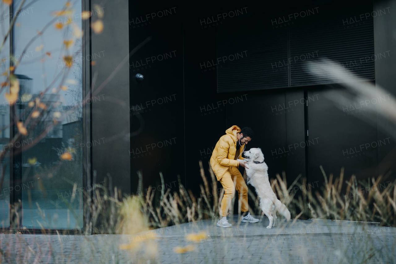 A happy young man playing with his dog during walk outdoors in city in winter.