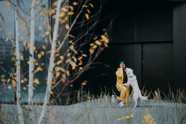 A happy young man walking and training his dog outdoors in city during autumn day.